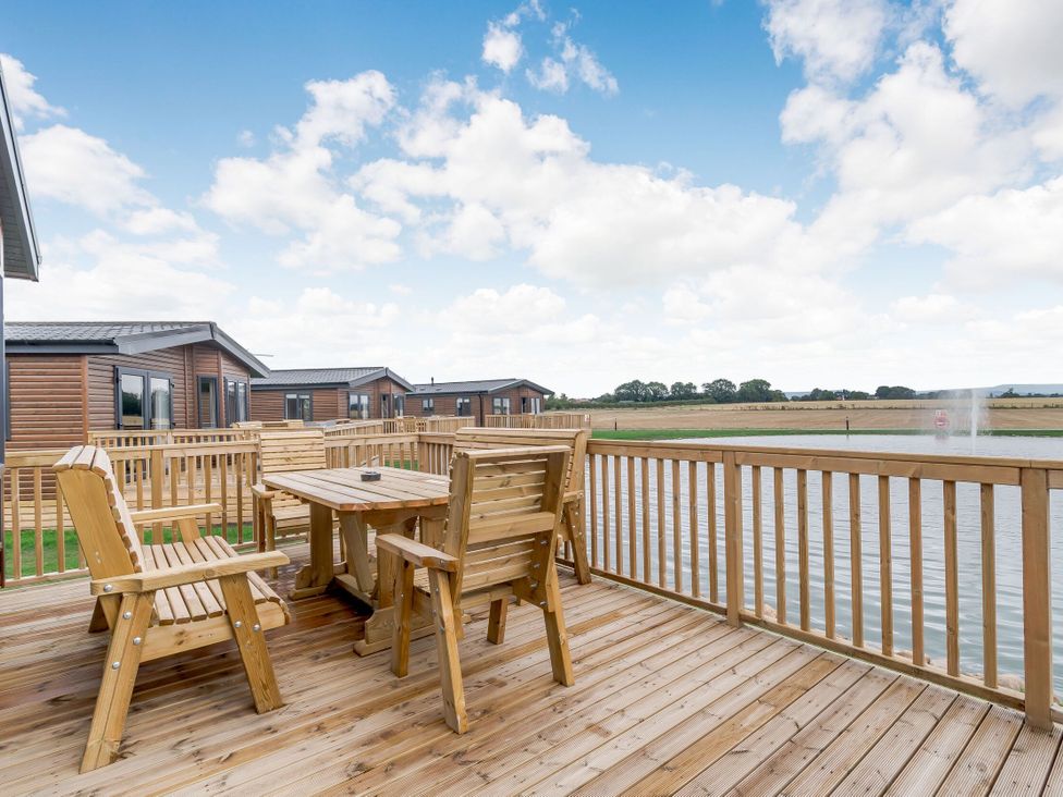 An outdoor area with wooden furniture and a view of a pond at Beech Waterside Spa (Pet) Carlton Miniott near Thirsk