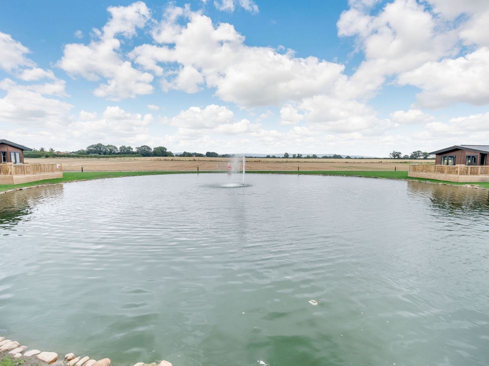 An outdoor area with a pond and two cabins at Beech Waterside Spa (Pet) Carlton Miniott near Thirsk