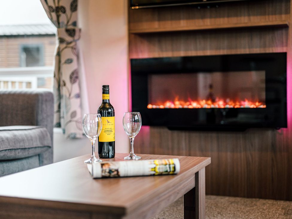 A living room with a sofa, table, wine bottle and glasses at Larch Waterside Spa (Pet) Carlton Miniott near Thirsk