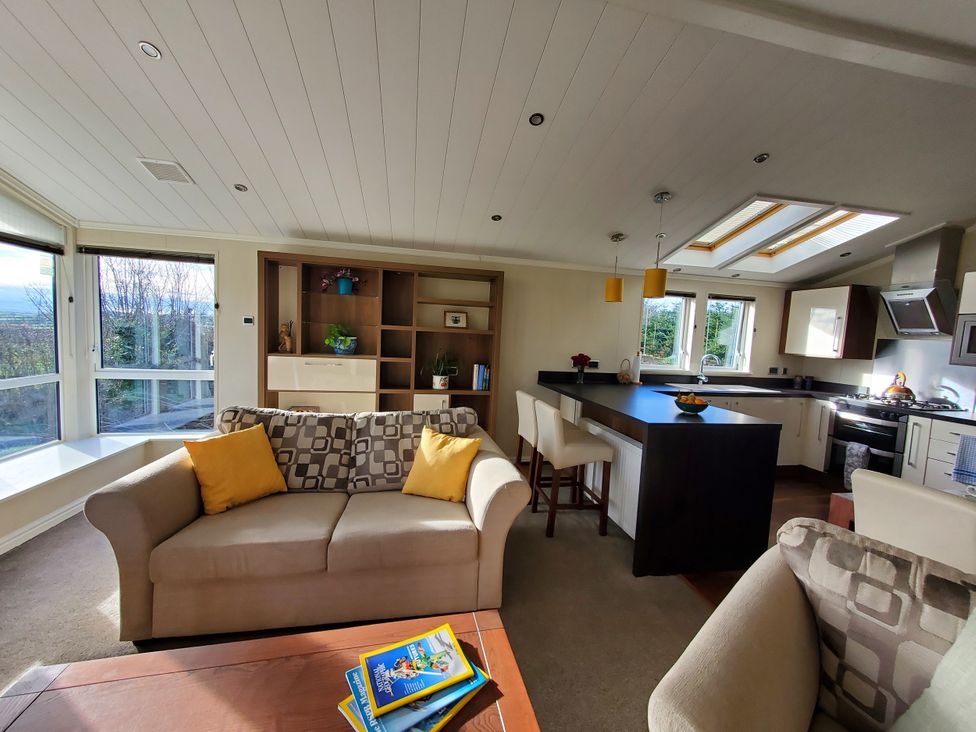 A living room with a sofa and kitchen area at Plas Marchog Lodge in Pentraeth