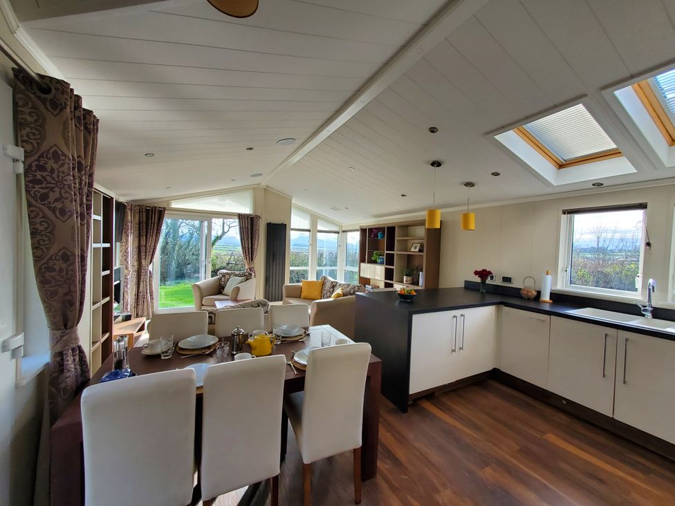 A living room and kitchen area with dining table and sofas at Plas Marchog Lodge in Pentraeth