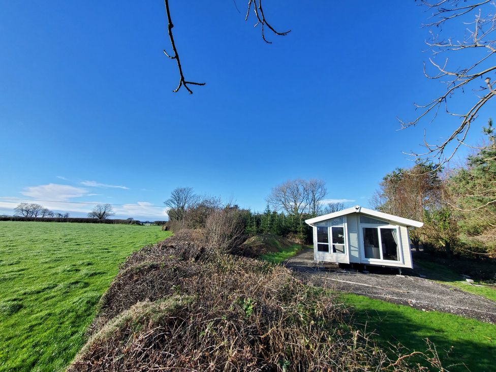 An outdoor view of a house with grass and trees at Plas Marchog Lodge in Pentraeth