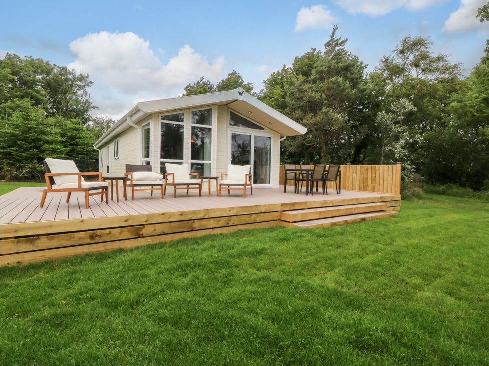 A house with a deck and chairs in a garden at Plas Marchog Lodge Rhoscefnhir near Pentraeth
