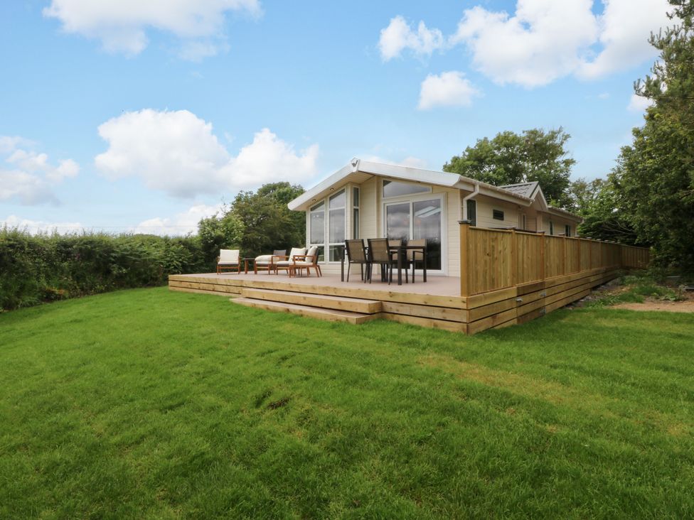 An outdoor area with a lodge and deck seating at Plas Marchog Lodge in Rhoscefnhir near Pentraeth