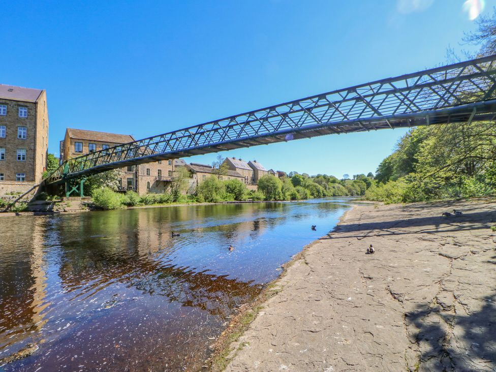 A river with a footbridge and buildings near the water at Mains Cottage in Consett