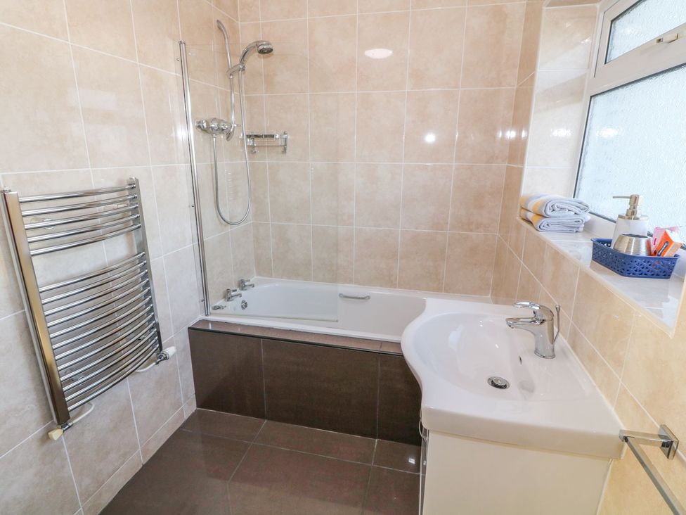 A bathroom featuring a bathtub, shower, towel rack, and sink at Dunholme