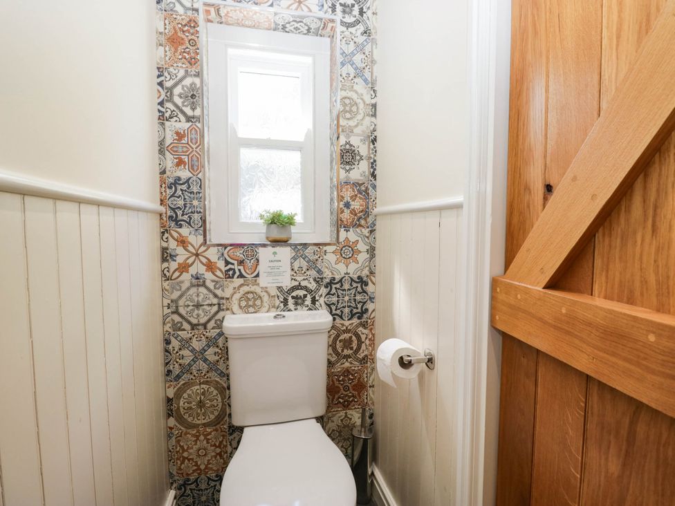 A bathroom with a toilet and patterned wall tiles at Cragg Cottage in Coniston