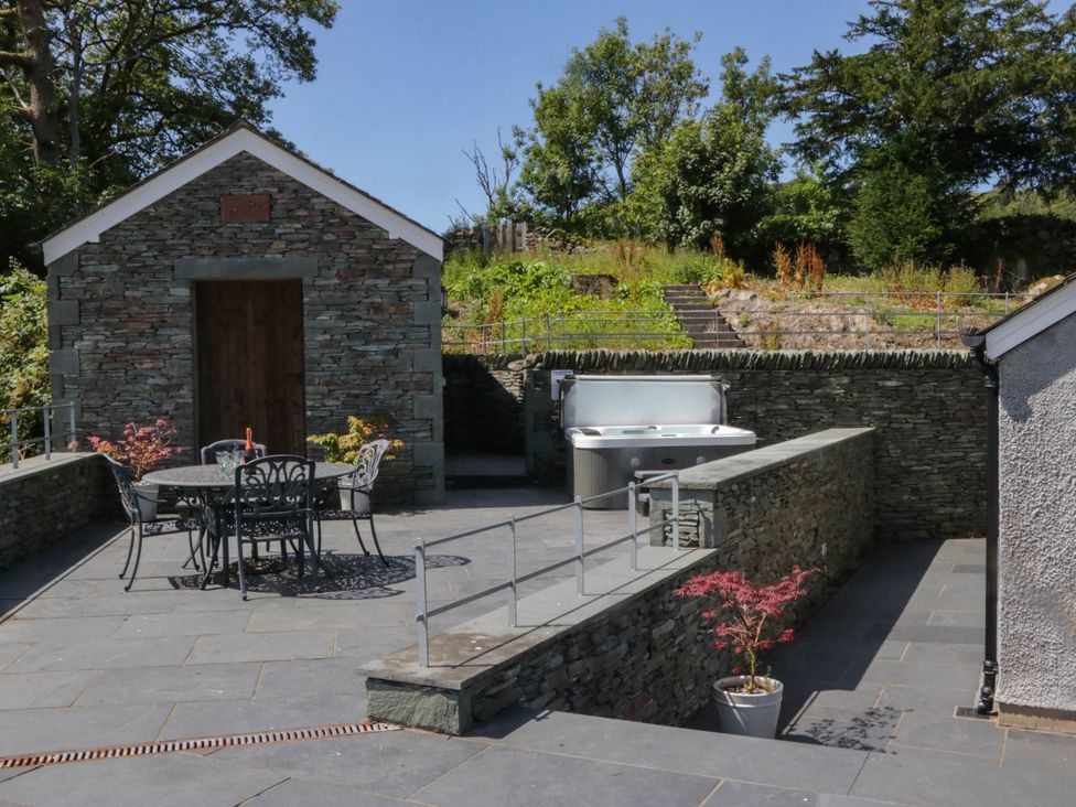 An outdoor area with a stone building, table and chairs, hot tub at Cragg Cottage in Coniston