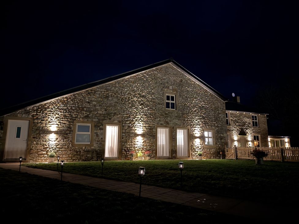 An outdoor view of a stone house with lights at The Barn Wigglesworth near Settle