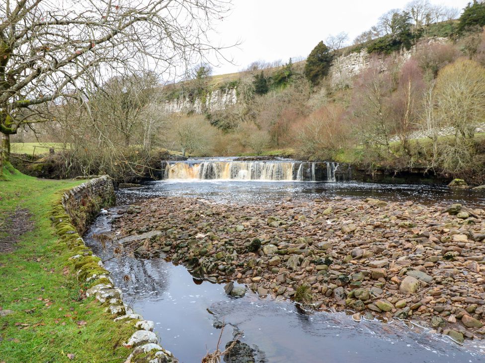 A waterfall cascading into a river with rocky banks and trees nearby at Wain Wath Cottage Richmond