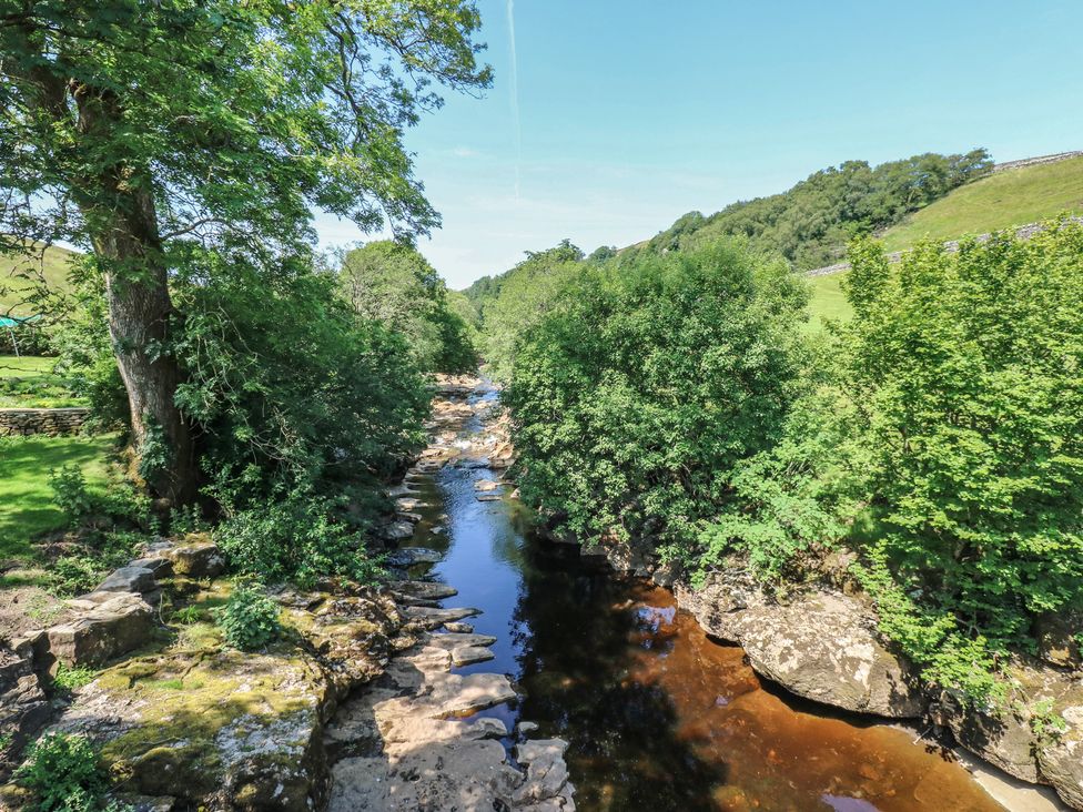 A river flowing through a landscape with trees and rocks at Wain Wath Cottage Keld near Muker