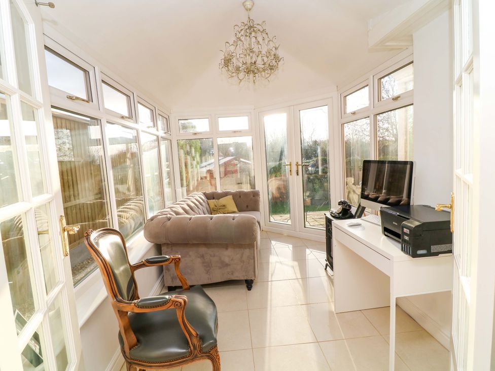 A conservatory with a sofa, chair, television and desk at 12 Wyndham Road in Loughborough