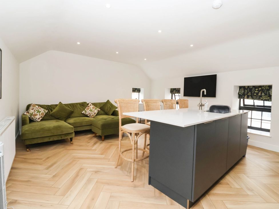 A living room with a green sofa and a kitchen island at The Old Bakehouse in 