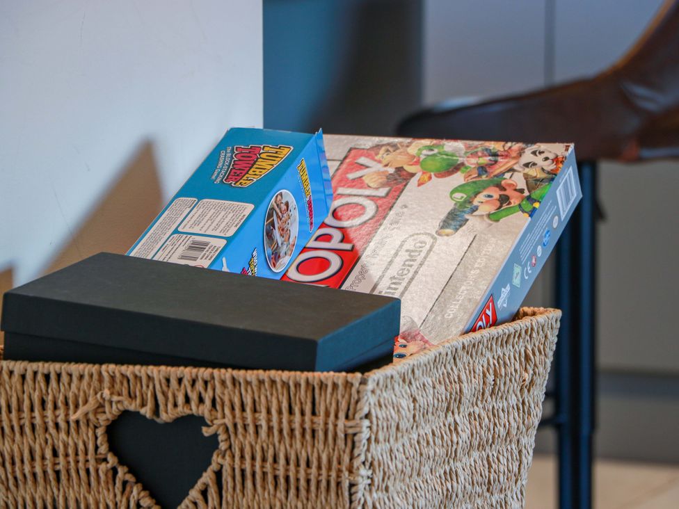 A storage basket with board games including Monopoly and a black box at Cramar Cottage in 