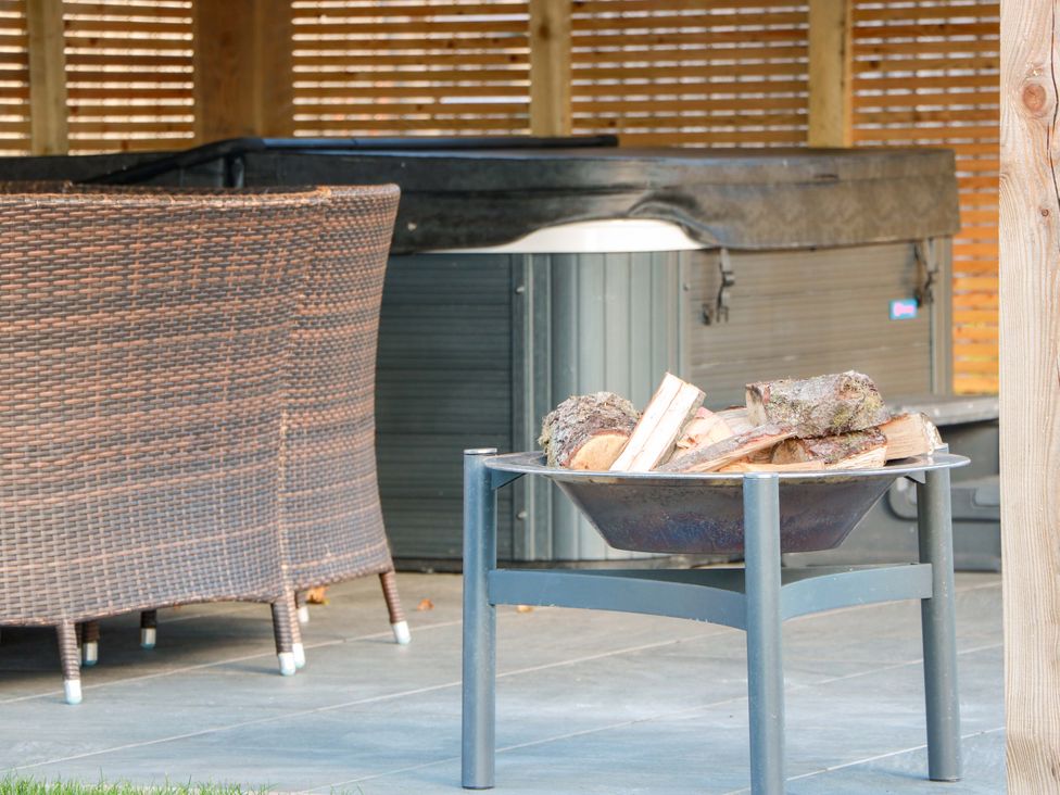 An outdoor space with a fire pit and logs near a hot tub at Cramar Cottage