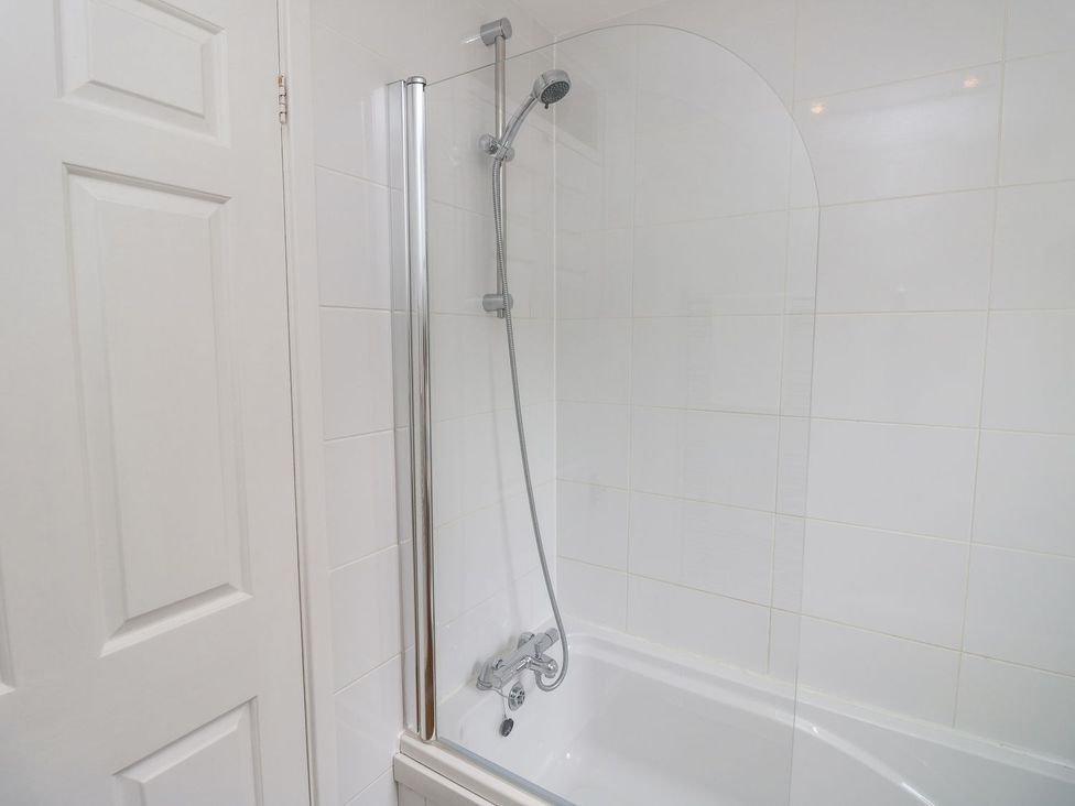 A bathtub with shower and wall tiles at Harbour View Poole