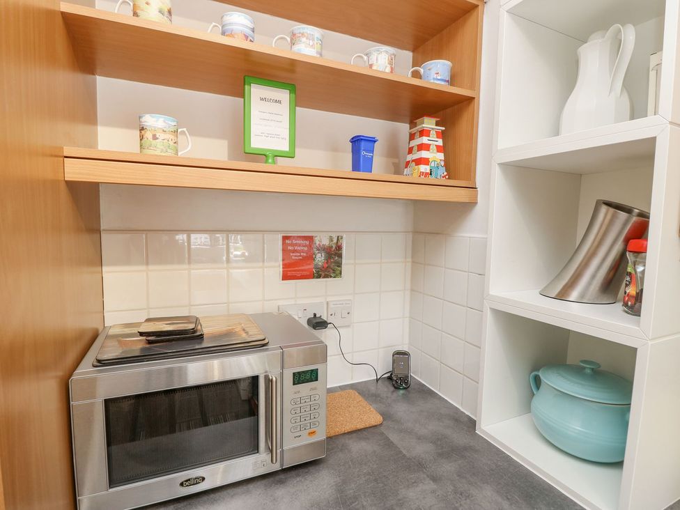 A kitchen with a microwave and mugs on a shelf at Poole Quay Cottage in Poole