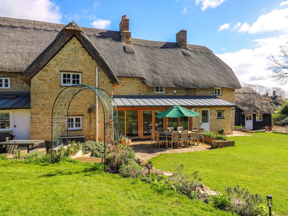 A garden with a thatched roof house and patio seating at Manor Farm Cottages in Loughton, Milton Keynes