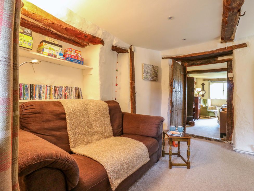 A living room with a sofa and shelf containing games at Manor Farm Cottages in Loughton, Milton Keynes