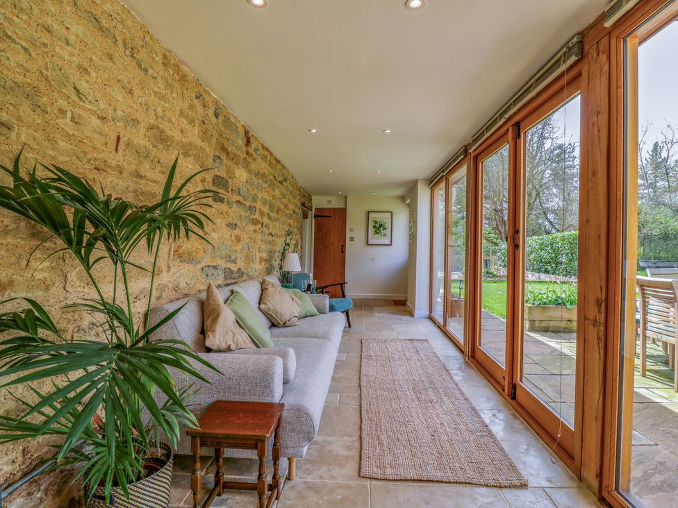 A conservatory with a sofa and large windows at Manor Farm Cottages, Loughton, Milton Keynes