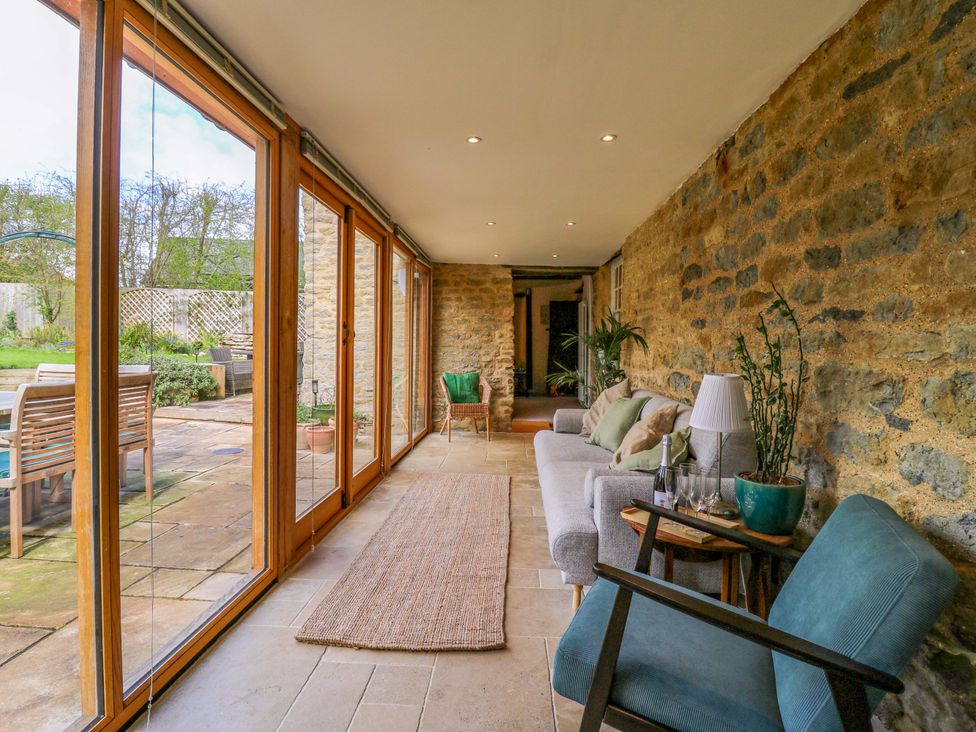 A conservatory with a sofa and armchair at Manor Farm Cottages in Loughton, Milton Keynes