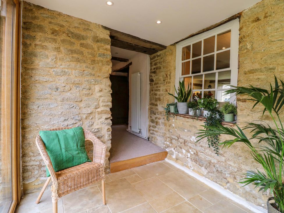A conservatory with a wicker chair and plants at Manor Farm Cottages Loughton, Milton Keynes