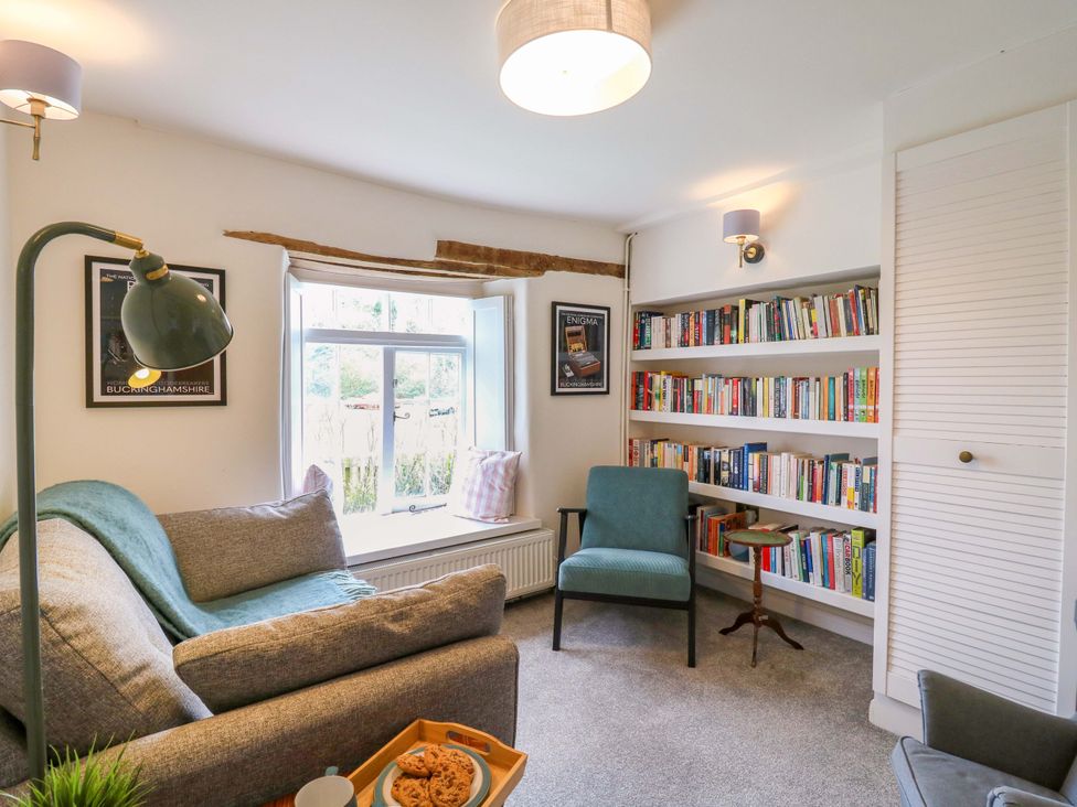 A snug room with a sofa, bookshelf and window at Manor Farm Cottages Loughton, Milton Keynes