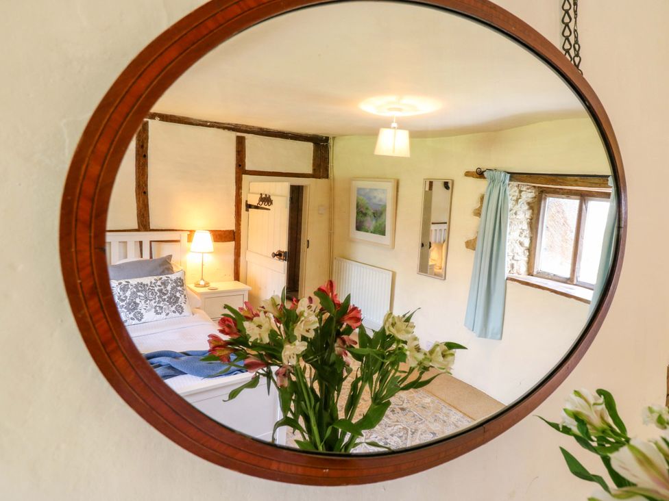 A bedroom with a mirror, bed, flowers and lamp at Manor Farm Cottages, Loughton, Milton Keynes