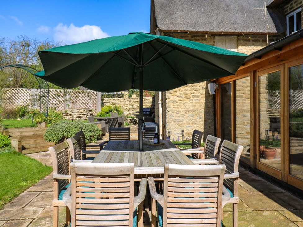 A dining area with a table and chairs under an umbrella at Manor Farm Cottages, Loughton, Milton Keynes