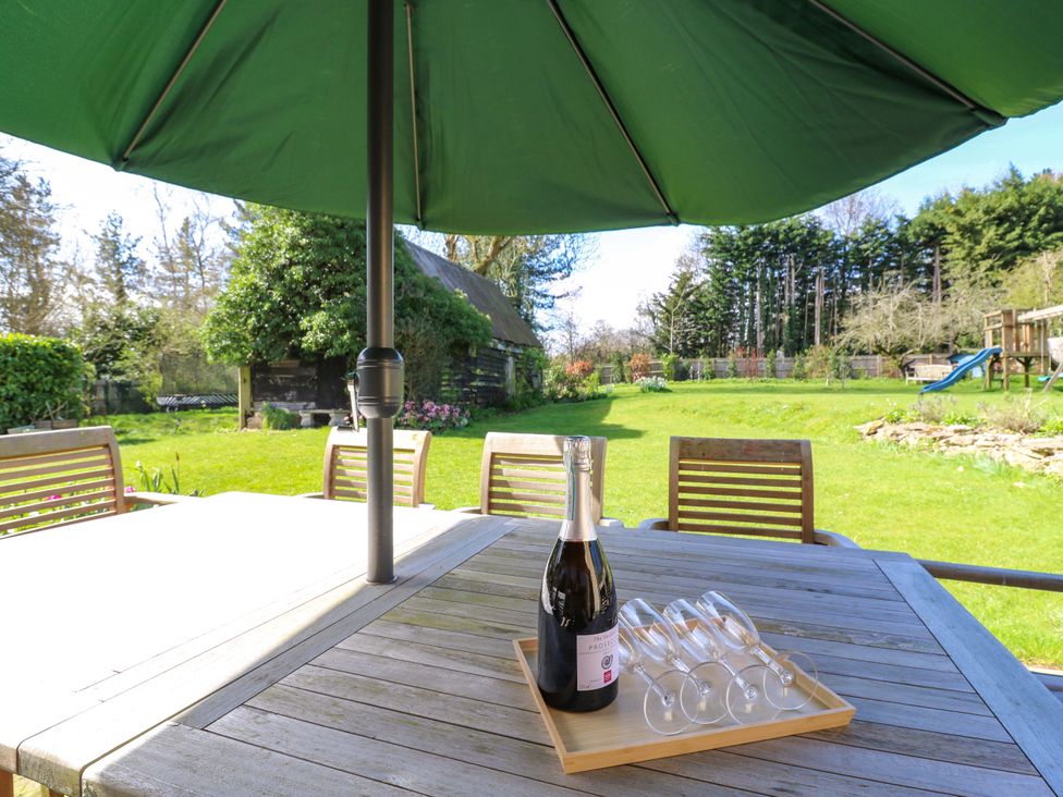 A table with a bottle and glasses under an umbrella at Manor Farm Cottages in Loughton, Milton Keynes