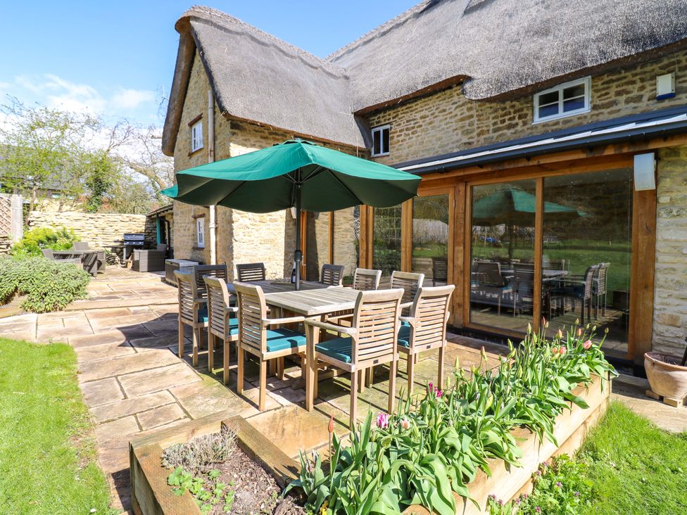 A patio with a table and chairs under an umbrella at Manor Farm Cottages, Loughton, Milton Keynes