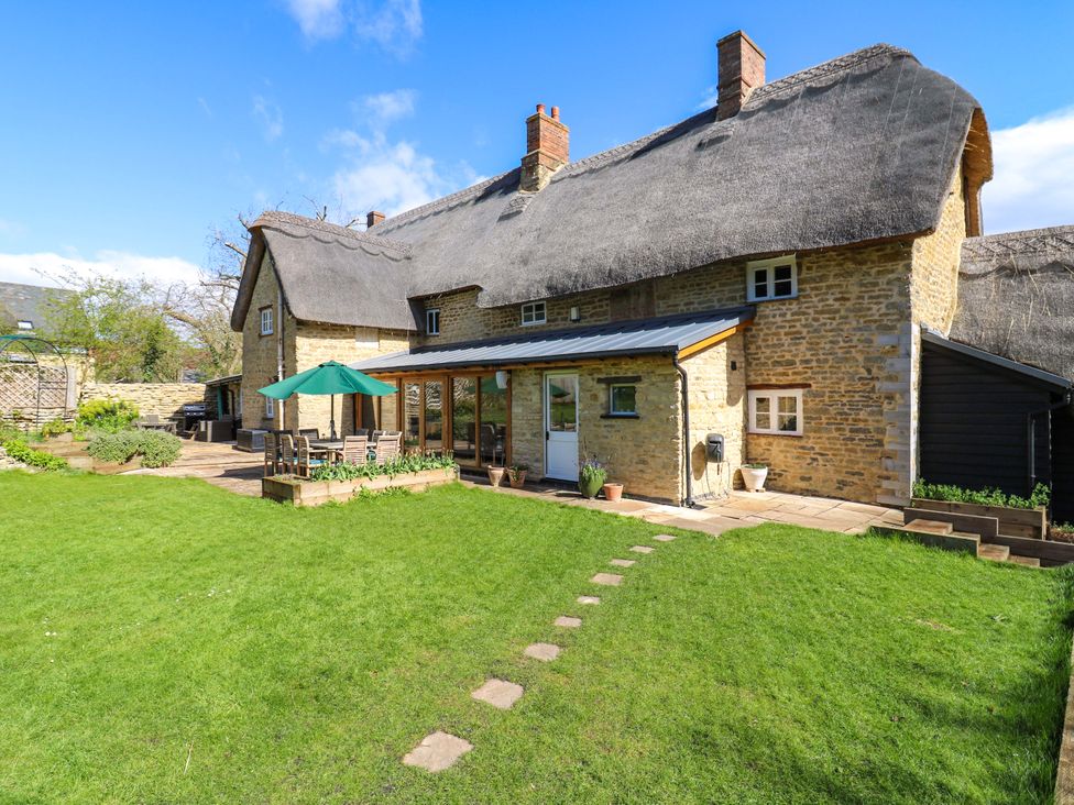 A garden with a stone house and patio area at Manor Farm Cottages in Loughton, Milton Keynes