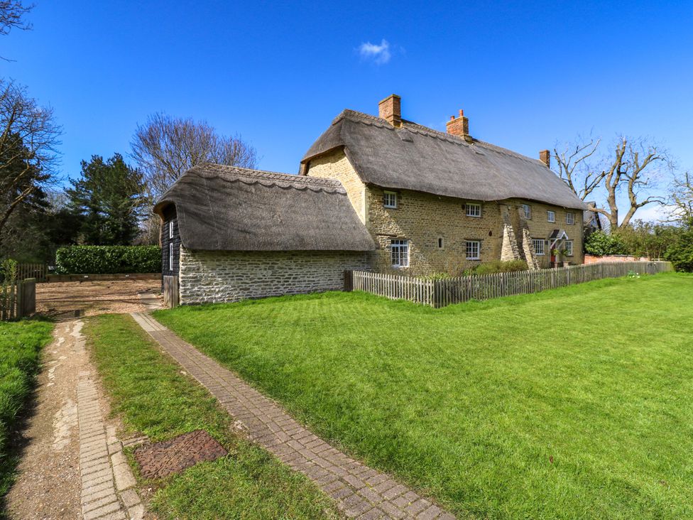 An exterior view of a thatched cottage with a garden at Manor Farm Cottages in Loughton, Milton Keynes