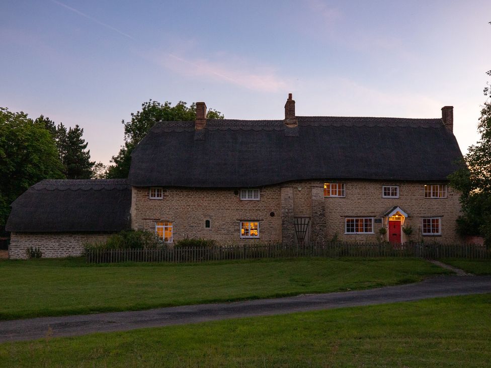A thatched roof house with a garden at Manor Farm Cottages in Loughton, Milton Keynes