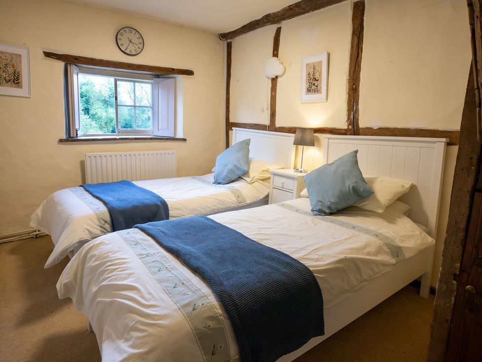 A bedroom with two beds, a lamp, and a window at Manor Farm Cottages Loughton, Milton Keynes