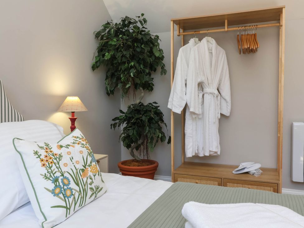 A bedroom with bed, lamp, and hanging robes at Captains Barn Tiverton