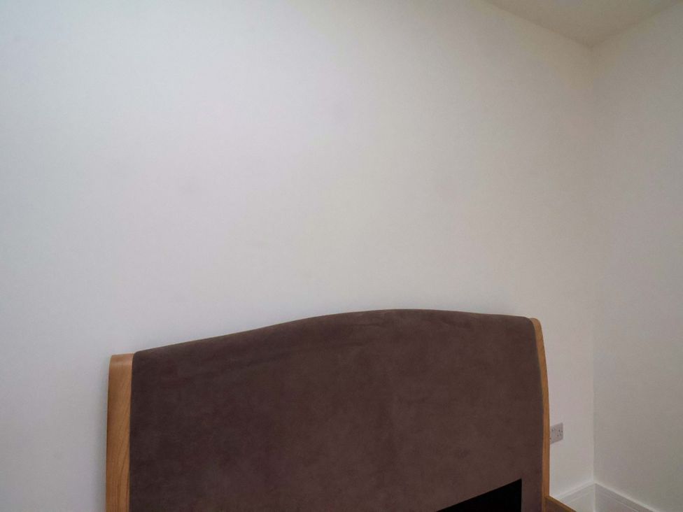 A bedroom with a headboard and a white wall at Beachwalk Villa 2 in Whitby