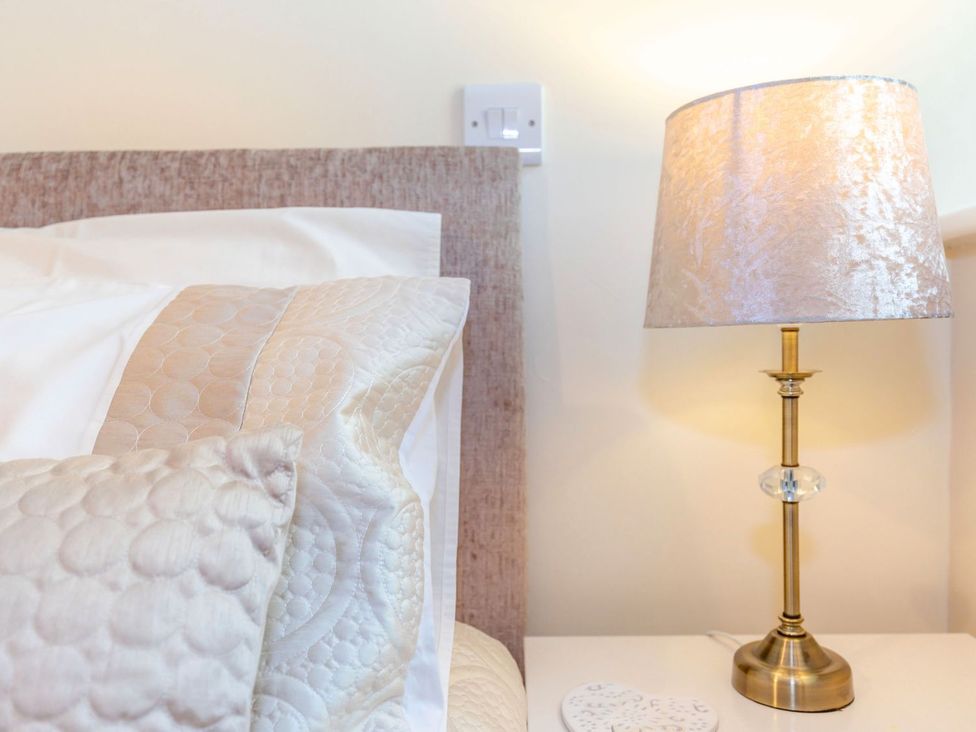 A bedside table with a lamp and pillows at Lanes Barn Whitby