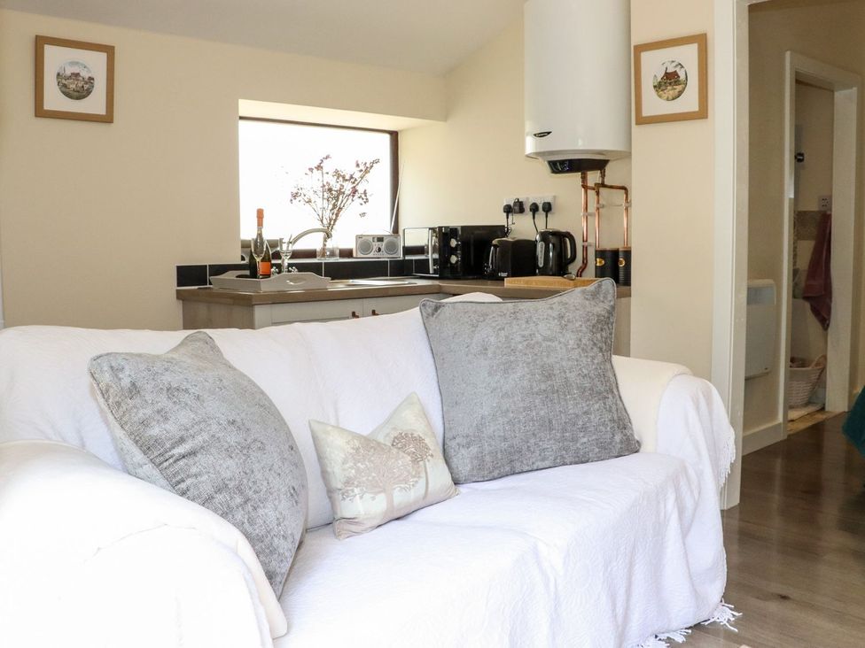 A living room with a sofa and kitchen area at Lannlyvri Lodge Lanlivery near Lostwithiel