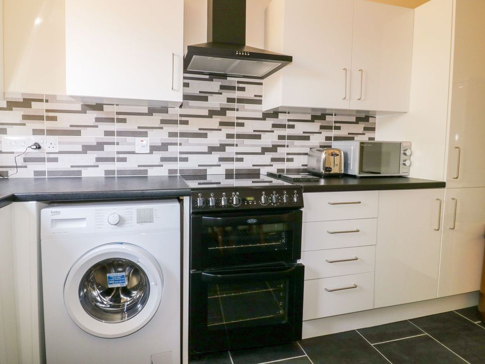 A kitchen with appliances including a washing machine, oven, and microwave at Camellia Cottage in Bodmin