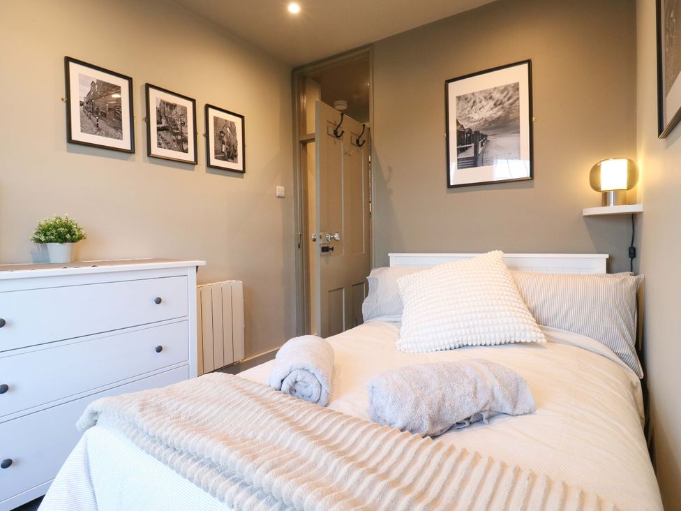 A bedroom with a bed and framed photographs at 1A Coastguard Cottages in Rye