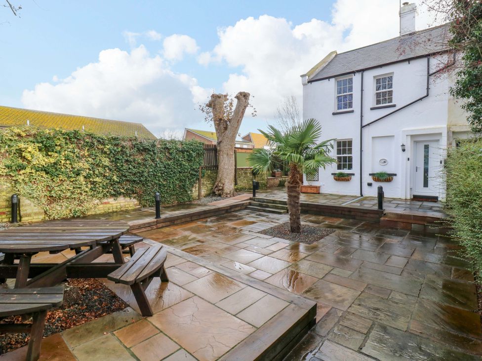 A garden with a patio table and palm tree at 1A Coastguard Cottages in Rye