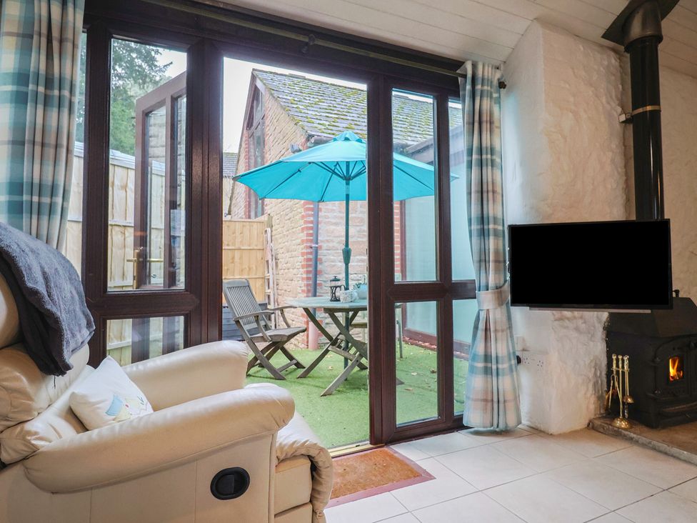 A conservatory with an armchair and a table with umbrellas at Apple Cottage Whitchurch Canonicorum
