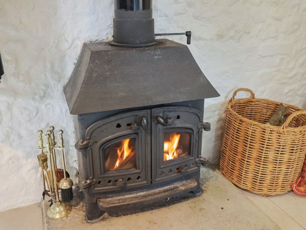 A wood stove with fire and a log basket at Apple Cottage in Whitchurch Canonicorum