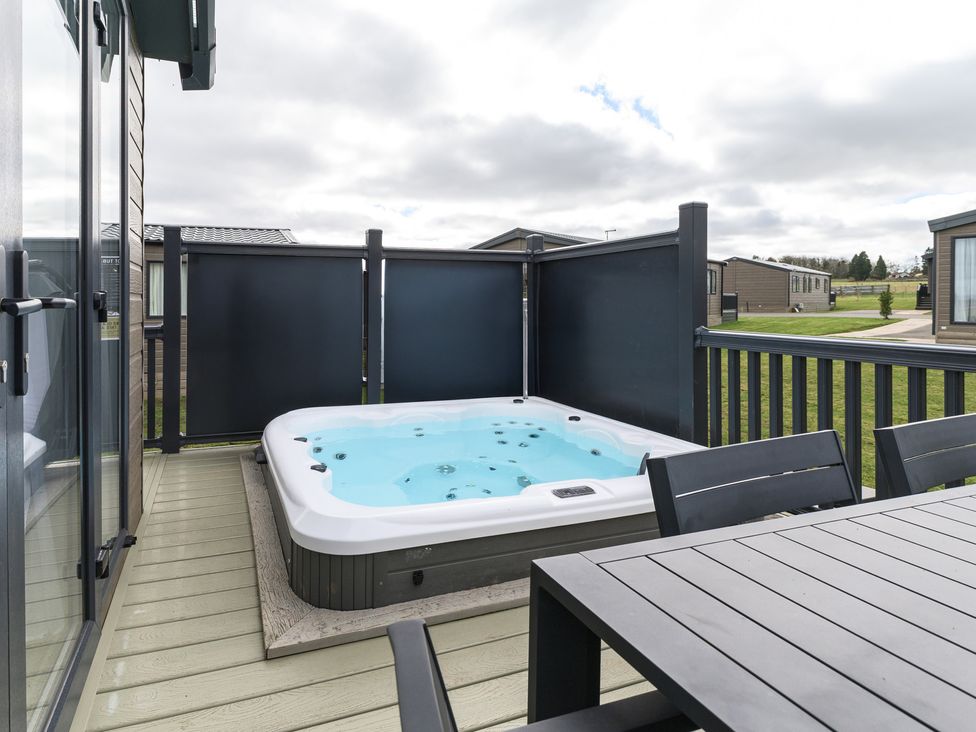 A hot tub on a patio with a table and chairs at Blencathra Spa (Pet) in Penrith