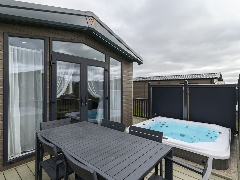 An outdoor patio with a dining table and hot tub at Blencathra Spa (Pet) Penrith