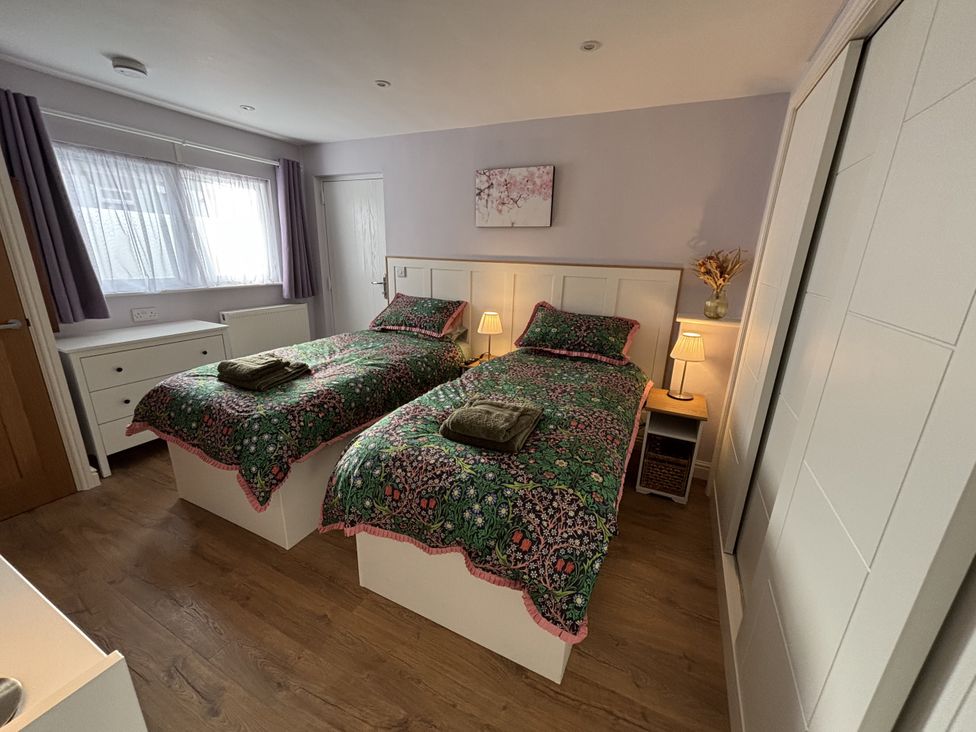 A bedroom with two beds and a bedside table at Drapers Cottage in Cark In Cartmel