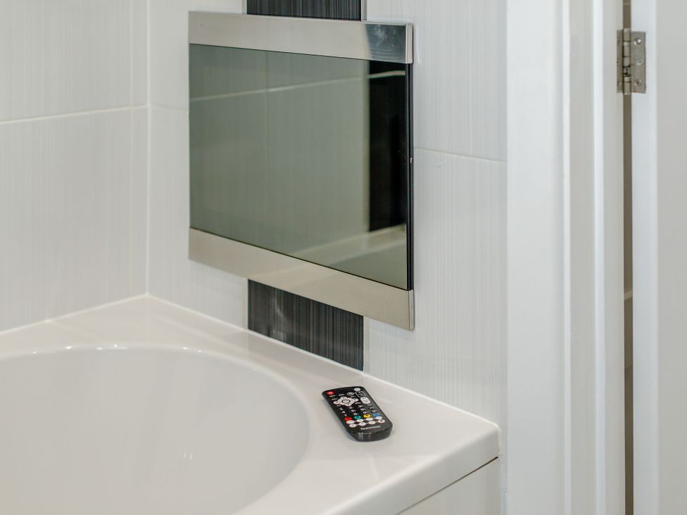 A bathtub with a remote control beside a wall-mounted mirror at Signature Assisted Living Pet in Portreath
