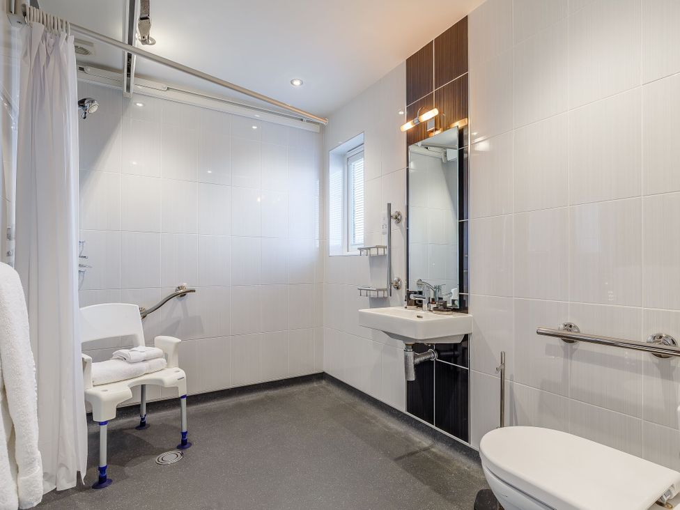 A bathroom with sink, toilet, shower, and safety chair at Signature Assisted Living Pet in Portreath