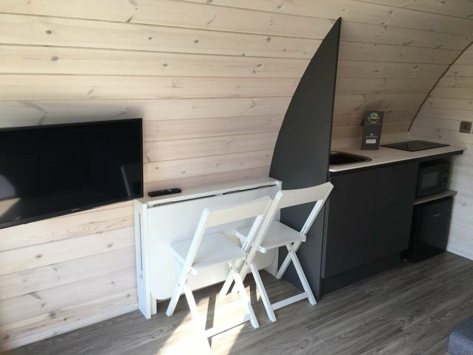 A kitchen with a television, a folding table with chairs, and appliances at Pod 9 (No Pets) in Carnforth